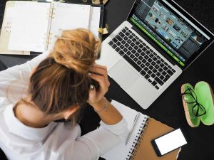 A woman with her head in her hands sat at a desk in front of a laptop